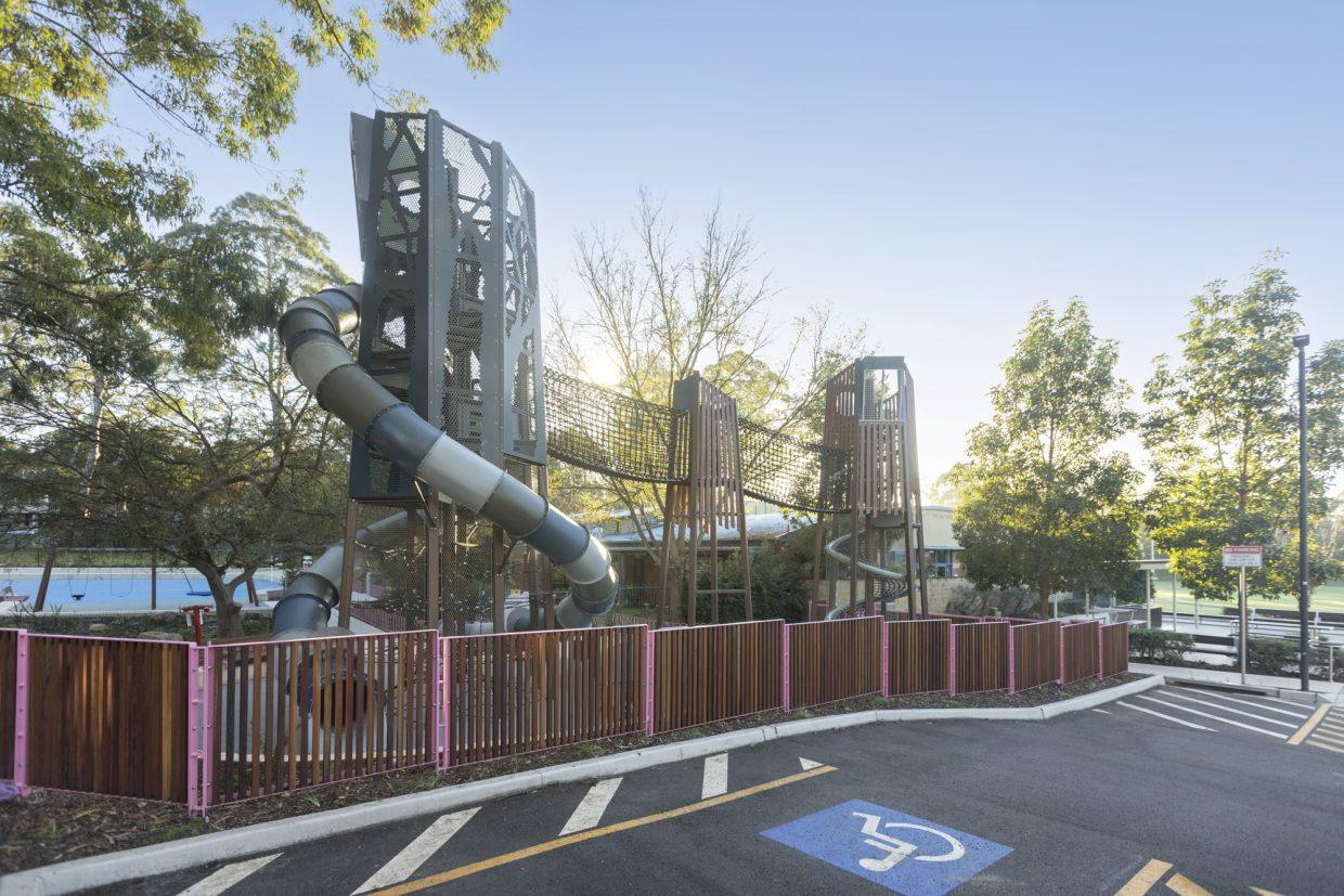 Somerville Park playground towers, enclosed rope bridge and tube slide beside an accessible parking bay.